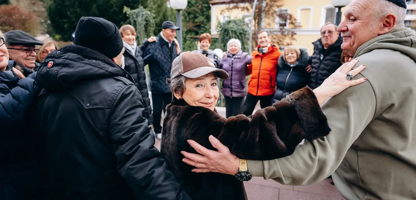 Senioren stehen im Kreis und eine Frau lächelt in die Kamera